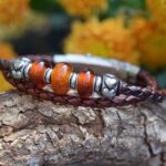 Men’s memorial bracelet with braided brown leather strap and transparent ashes bead between brown glass spacers.
