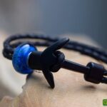 Memorial bracelet with black leather strap and transparent blue glass bead containing visible cremation ashes.