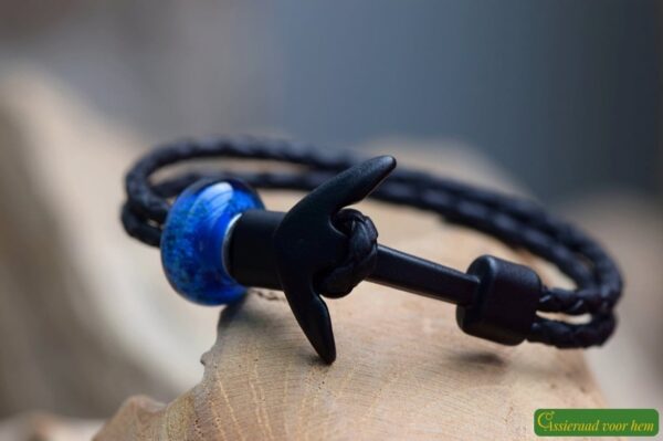 Memorial bracelet with black leather strap and transparent blue glass bead containing visible cremation ashes.