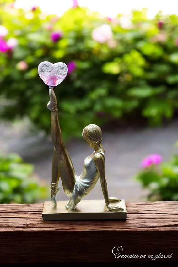 holding a glass heart on her toe with visible cremation ashes fused inside.