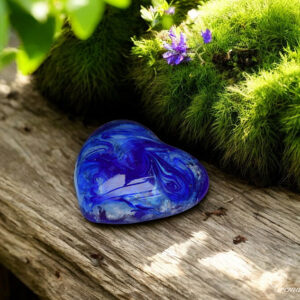 Blue-transparent glass heart with visible cremation ashes and mounting system to screw onto a sculpture or photo frame.
