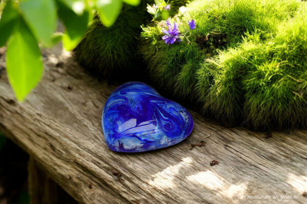 Blue-transparent glass heart with visible cremation ashes and mounting system to screw onto a sculpture or photo frame.
