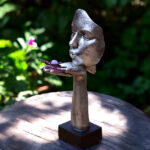 Silver-colored sculpture with face and hand