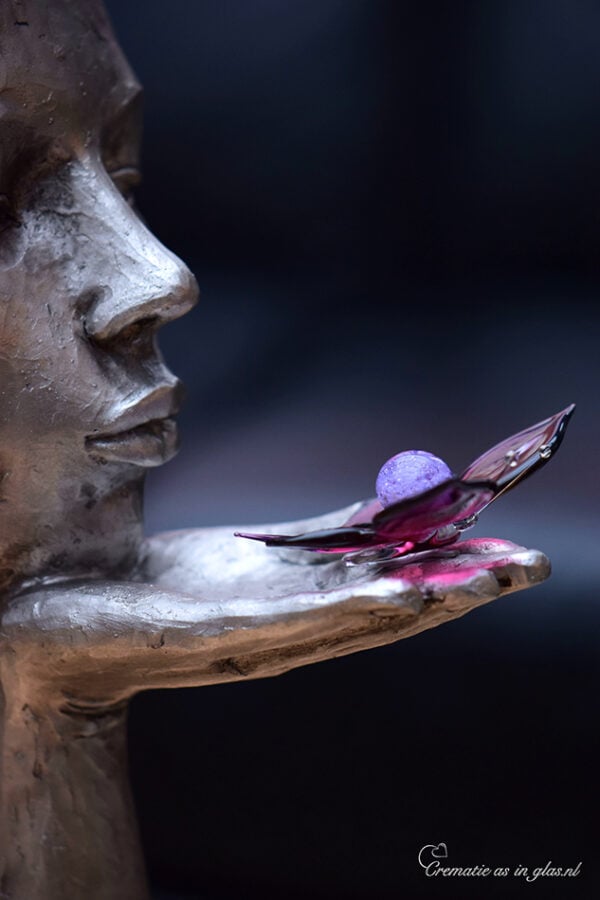 holding a purple glass butterfly with lilac mini urn containing visible cremation ashes.