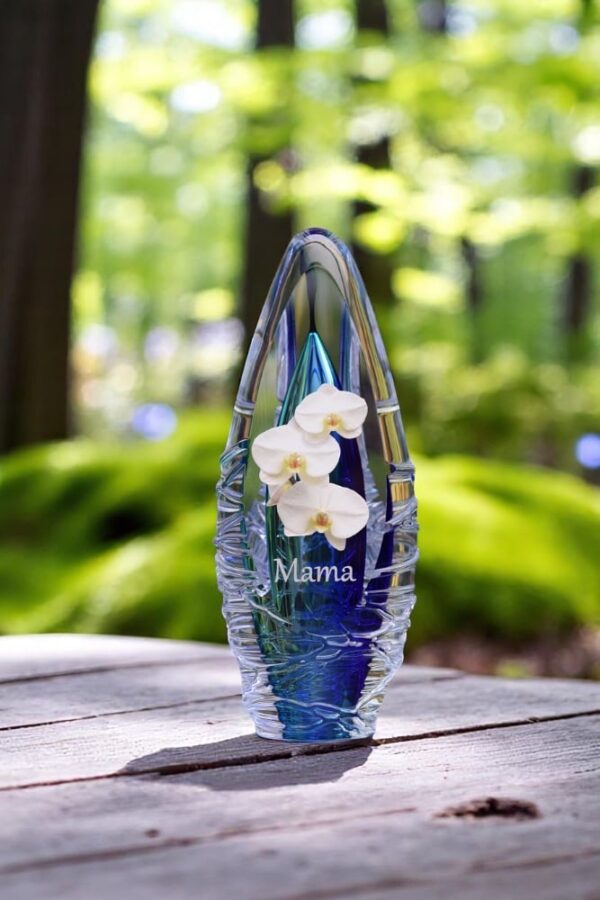 Design urn made of glass with transparent blue ash chamber and image of a white orchid – suitable for storing cremation ashes.