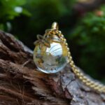 Memorial pendant with visible ashes in gold shimmering transparent glass and gold stainless steel bail.
