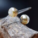 Minimalist memorial bangle with two semi-visible ashes beads in gold shimmer glass and surgical-grade stainless steel.