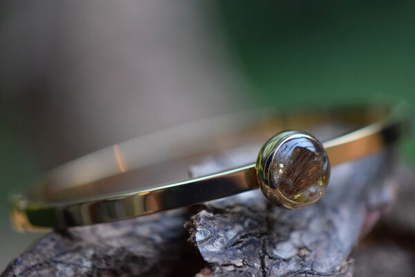 Gold-tone memorial bangle with visible hair or ashes on glass backing