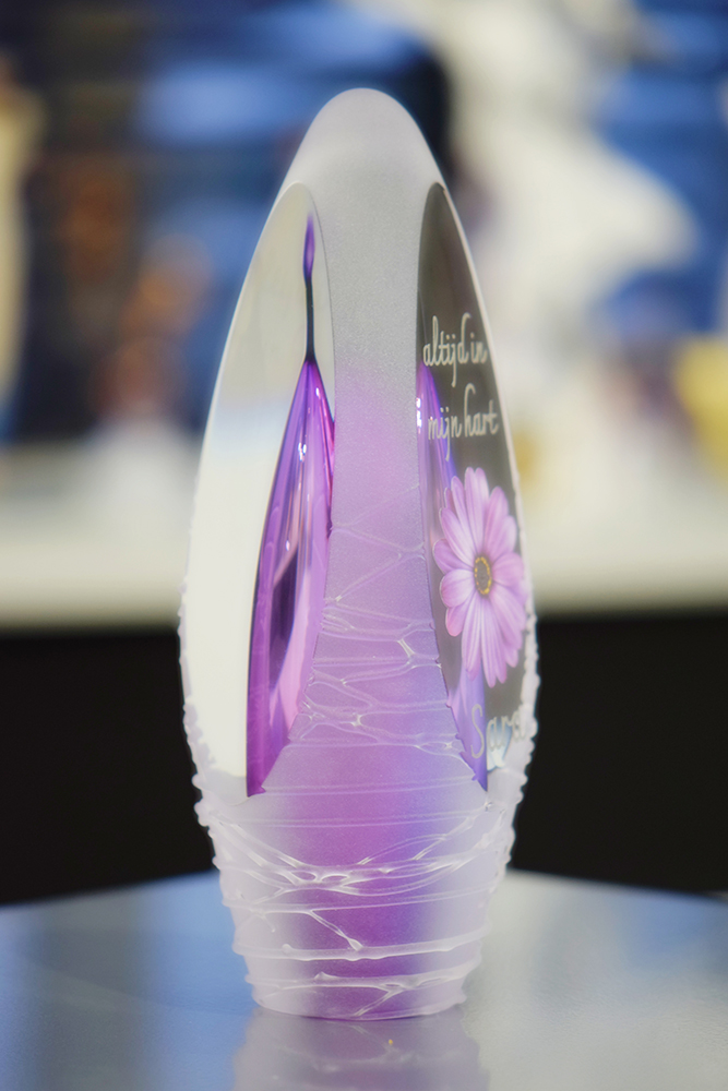 Glass design urn with transparent purple and pink ash chamber and image of a purple flower with space for a short name – suitable for cremation ashes.