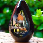 Designer urn made of glasss with green-yellow ash chamber and image of a robin on a branch with space for a short name - suitable for cremation ashes.