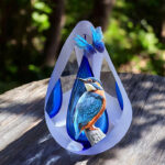 Designer urn made of glass with transparent blue ash chamber and image of a kingfisher with space for a short name - suitable for cremation ashes.