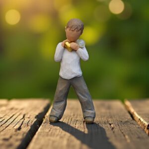 Willow Tree figurine Heart of Gold with boy holding a golden heart to his chest and a glass mini urn on his shoulder for ashes or hair.