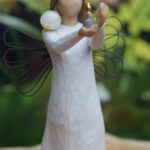 Willow Tree figurine Angel of Hope holding a small candle and a gold and transparent glass urn for ashes or hair as a symbolic memorial.