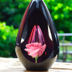 Designer urn made of glass with transparent pink ash chamber and image of a pink rose - suitable for cremation ashes.