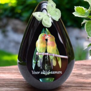 Design urn made of glass with transparent green-yellow ash chamber and image of two lovebirds – suitable for storing cremation ashes.