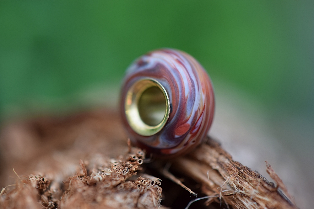 a cremation ashes glass bead in the colors red, brown and white