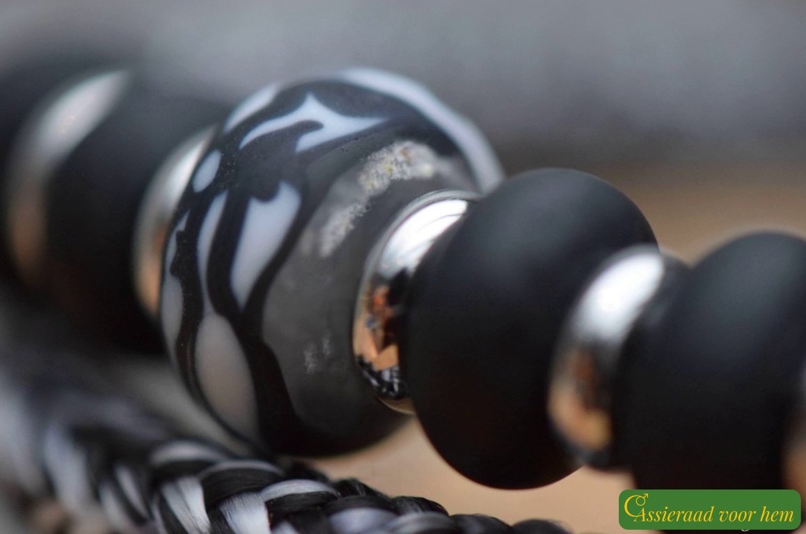 Detail of black-and-white cremation ashes glass bead between matte black glass beads and silver spacers.
